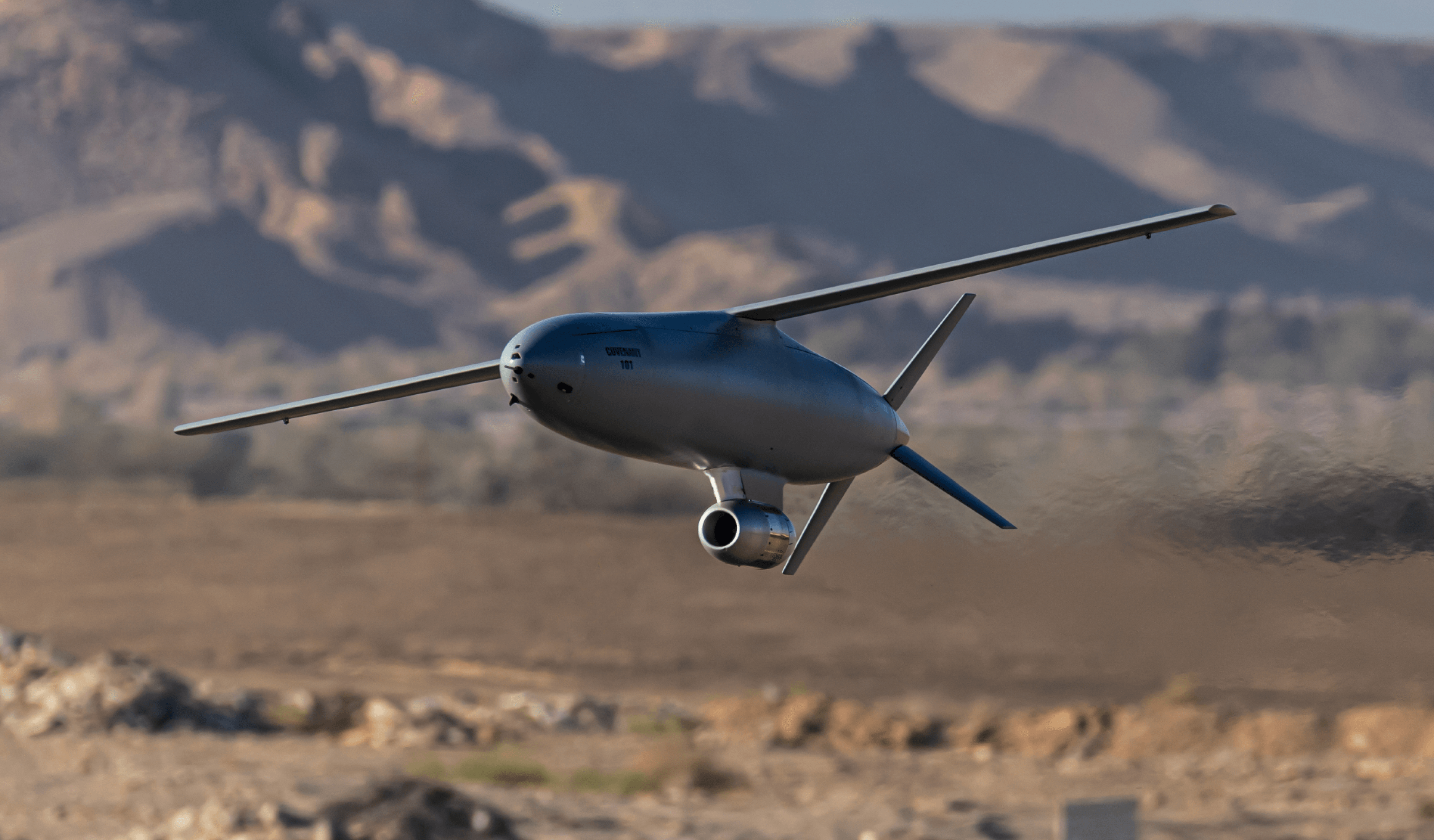 A Covenant cruise missile in level flight low over desert terrain, mountains behind it.